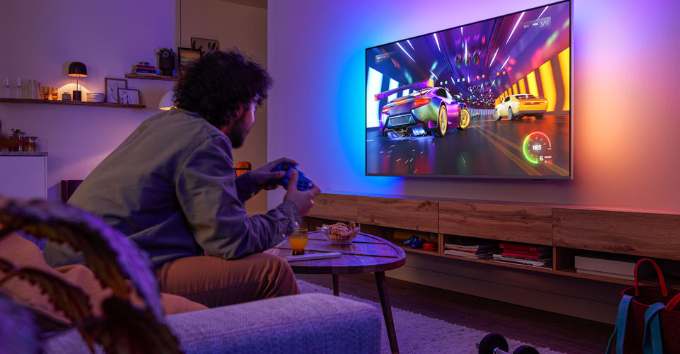 En person sitter i en sofa og spiller et racingspill p&aring; en Philips Ambilight-TV